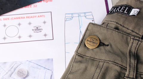 close up of front button on a pair of pants folded and laid on top of design plans